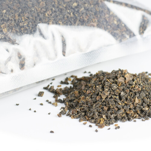 Trufo - Airdried Summer Truffle 2-4mm represented as air-dried black summer truffle particles partially spilled from a transparent vacuum-sealed pouch onto a white surface
